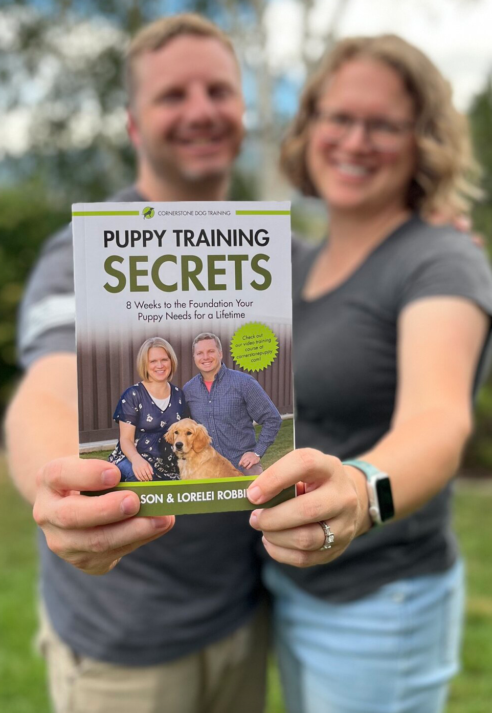 Jason and Lorelei Robbins, founders of Cornerstone Dog Training, smiling and holding their book "Puppy Training Secrets"—a complete guide to raising a well-trained puppy.